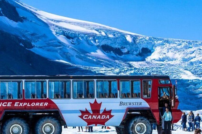 A red and white bus with 'ICE EXPLORER' and 'BREWSTER' written on it, parked in a snowy landscape with a mountain in the background. 4