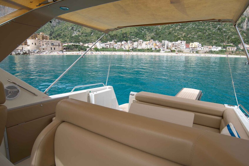 A boat's interior with beige leather seats and a view of a coastal town with buildings and a beach. 3