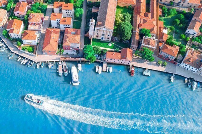 An aerial view of a coastal town with historic buildings, a marina with boats, and a clear blue sea. 4