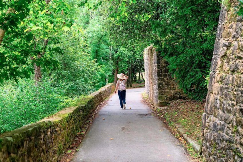 A person walking on a paved path surrounded by lush greenery and stone walls. 3