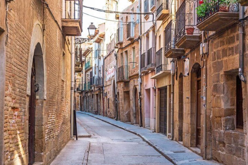 A narrow street lined with historic buildings, some with balconies and flower boxes. 5