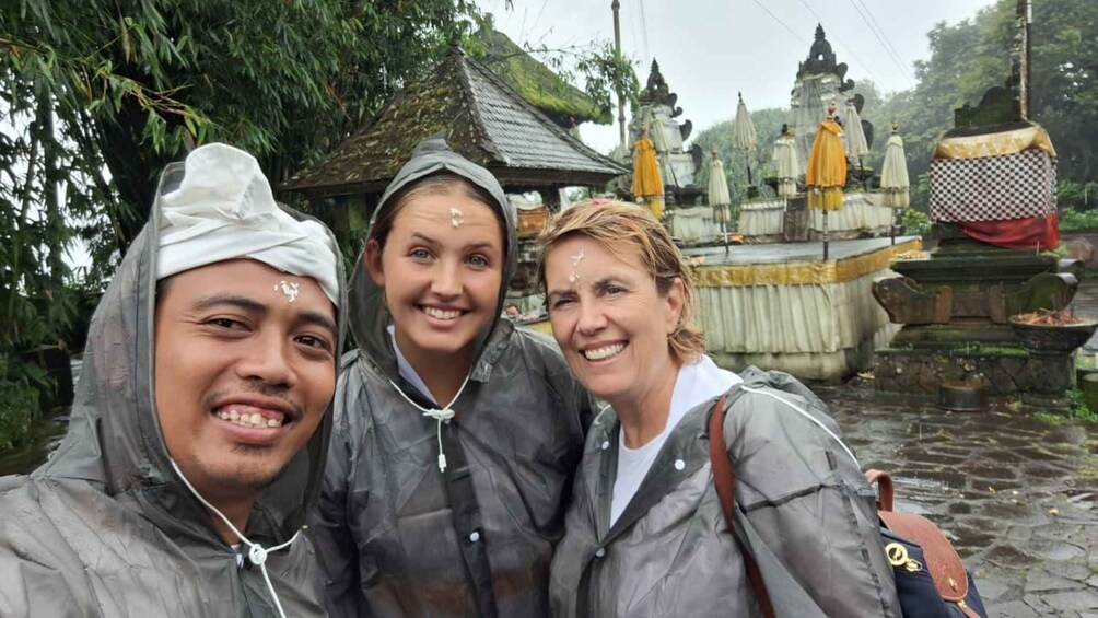 Three people in raincoats at a temple with statues and a stone structure. 3