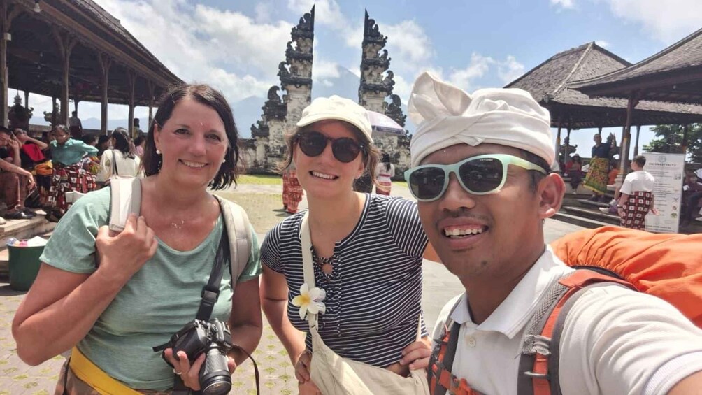 Three people taking a selfie with a temple and a thatched-roof structure in the background. 2