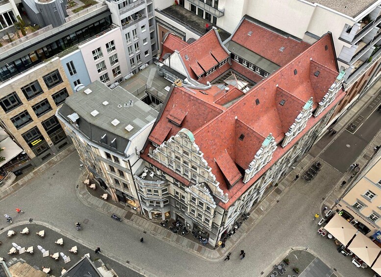 An aerial view of a historic building with a red-tiled roof, surrounded by modern buildings and a cobblestone street. 3