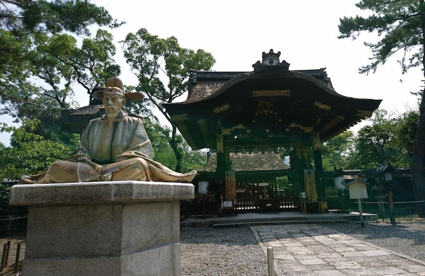 A stone statue of a seated figure in traditional attire, a pagoda-style structure, and a stone pathway leading to the structure. 4