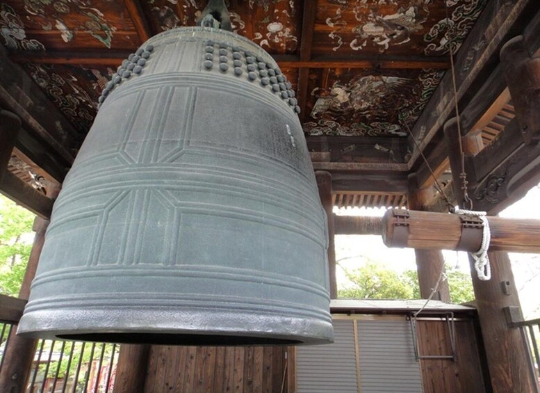 A large bell hanging from a wooden structure with intricate carvings on the ceiling. 5