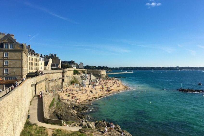 A coastal town with a fortified wall, a sandy beach, and calm blue waters. 3