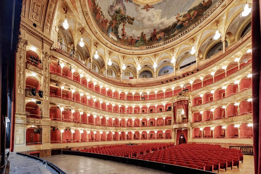 A grand theater with multiple balconies, ornate ceiling frescoes, and red seating. 3