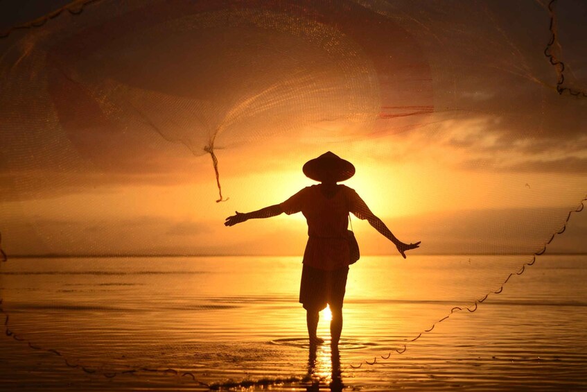 A person standing in shallow water with arms outstretched, silhouetted against a sunset. 1