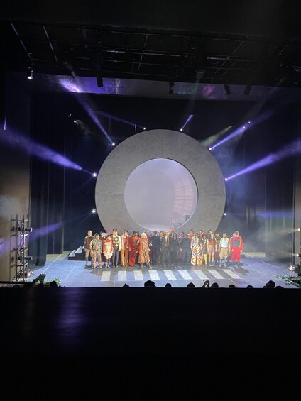 A group of people on a stage with a large circular backdrop and stage lighting. 5