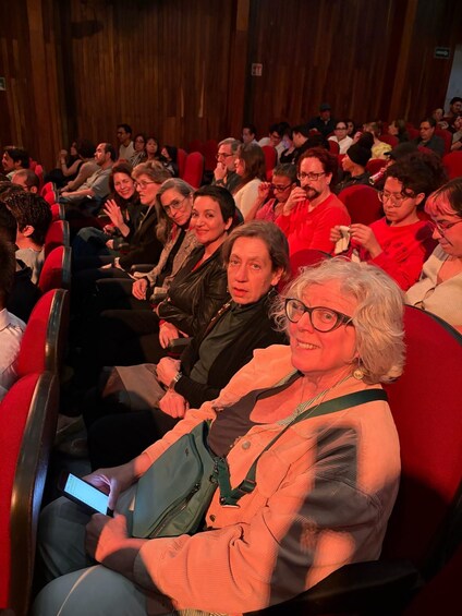 A theater audience seated in red chairs. 4