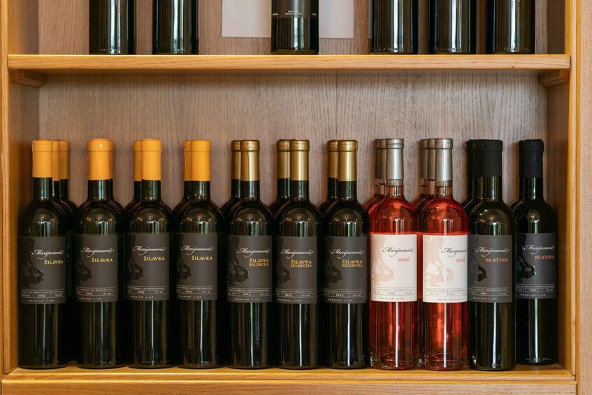 A wooden wine rack with bottles of Zilavka wine, including a rosé and Blatina varieties. 1