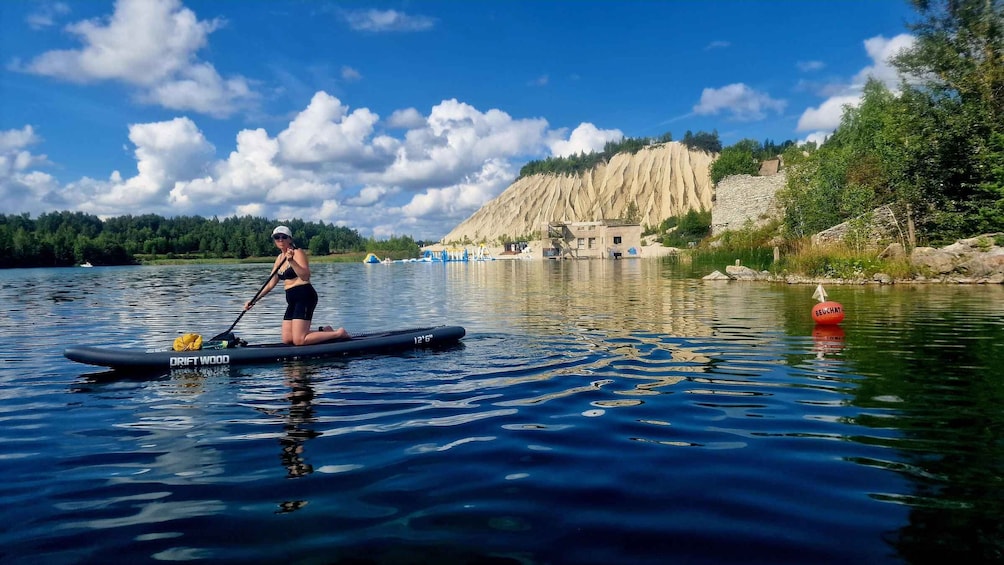 A person paddleboarding on a calm lake with a rocky cliff and trees in the background. 1