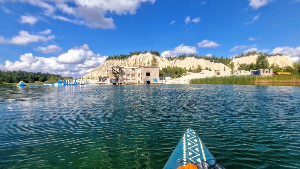 A calm lake with a kayak, a small dock, and a rocky cliff with buildings. 5