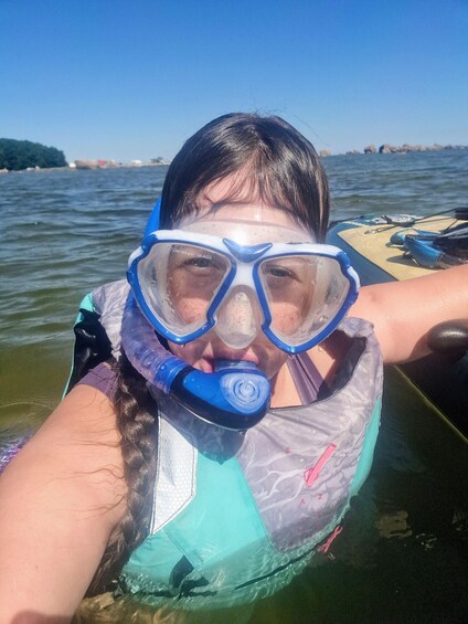 A person snorkeling with a mask and snorkel, wearing a life vest, in a body of water with a boat and distant shoreline. 2