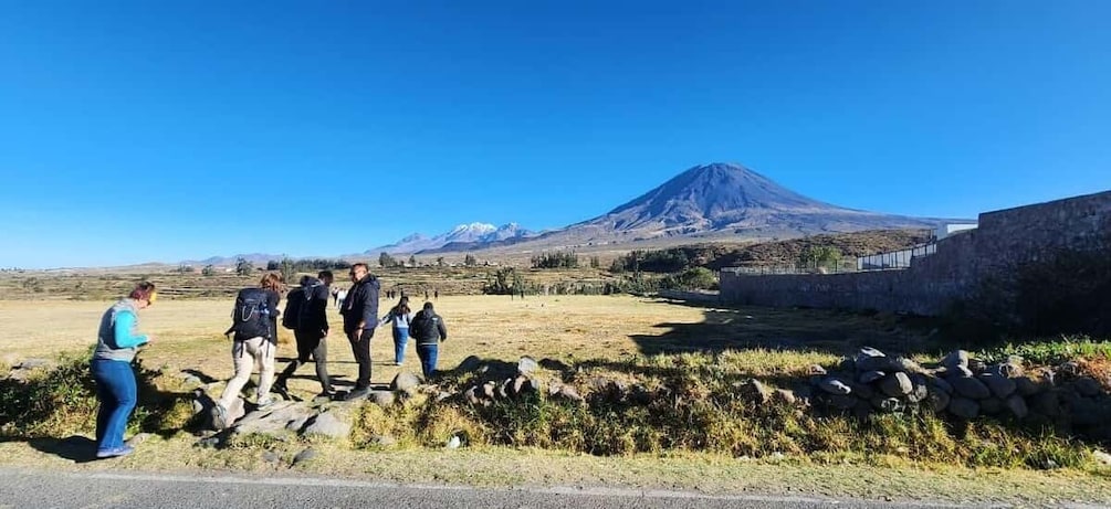 A group of people standing near a stone wall with a mountain in the background. 2