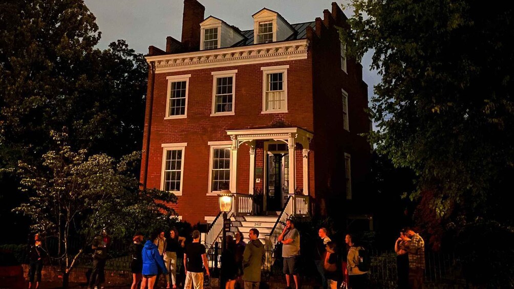 A historic brick building with a porch and a crowd gathered in front. 2