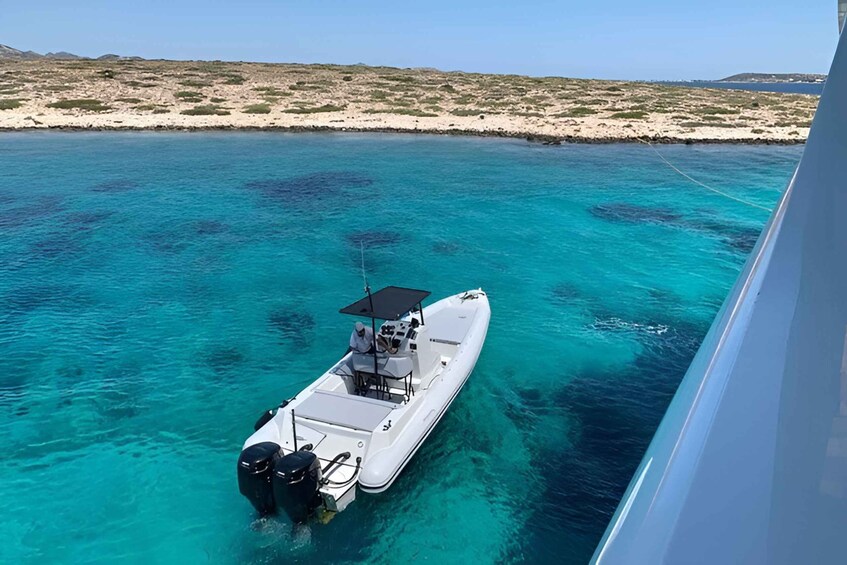 A white boat anchored in clear turquoise waters with a sandy beach and sparse vegetation in the background. 1