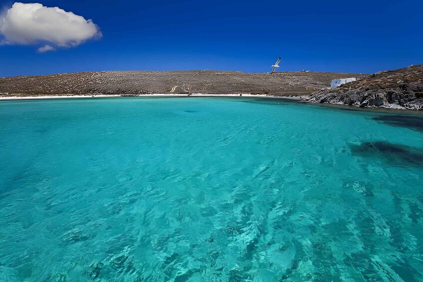 A clear turquoise sea, a white building, and a rocky hill with a wind turbine. 3