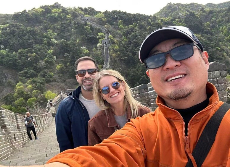 A person taking a selfie with a historic stone wall and a forested hill in the background. 3