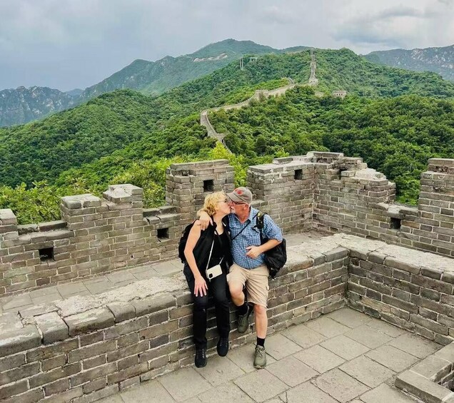 A couple sitting on the Great Wall of China with lush green mountains in the background. 4