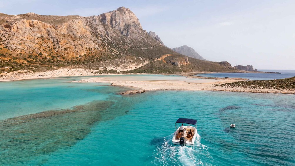 A boat on clear turquoise waters with a mountainous coastline in the background. 1
