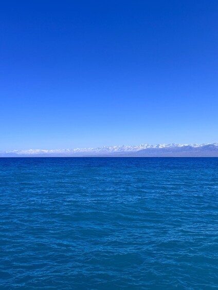 A calm sea with a clear blue sky and snow-capped mountains in the distance. 2
