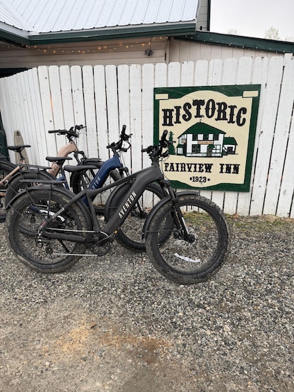 A gravel parking area with three bicycles parked in front of a white picket fence and a building with a sign that reads 'HISTORIC FAIRVIEW INN 1923.' 5