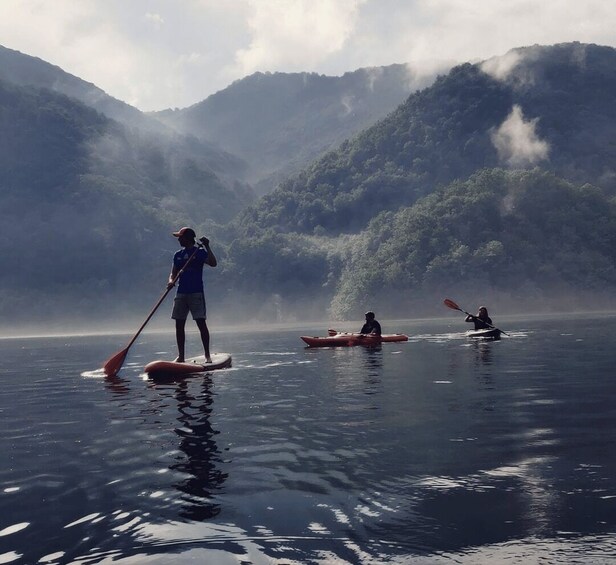 Three people kayaking on a calm lake surrounded by misty mountains. 2