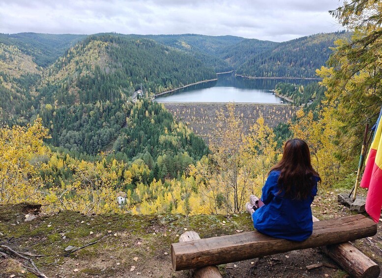 A person sitting on a log overlooking a lake surrounded by forested hills. 3