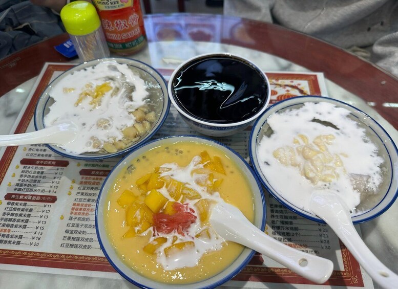 Three bowls of dessert with toppings, a bottle of sauce, and a menu with prices in a restaurant setting. 4