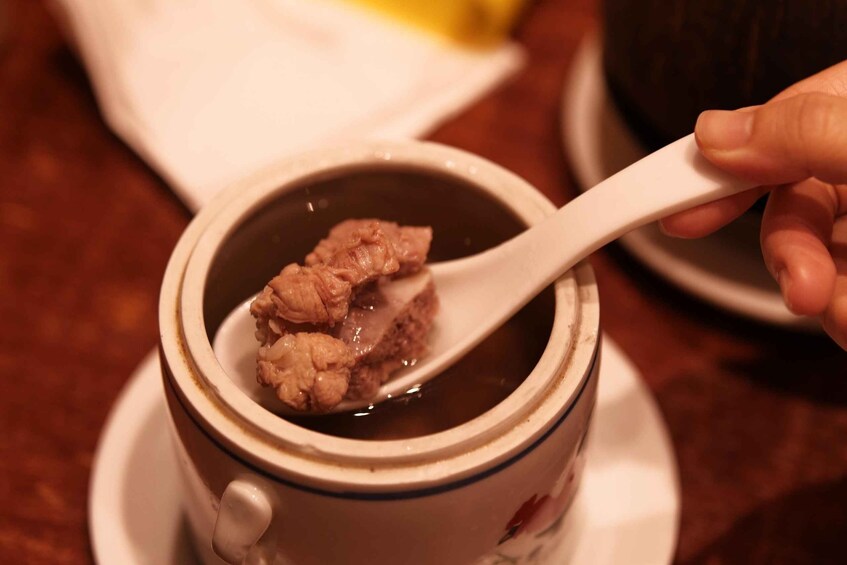 A hand holding a white spoon over a cup with a floral pattern, containing a brownish substance. 3