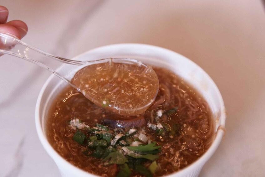 A bowl of soup with a clear spoon lifting a portion. 5