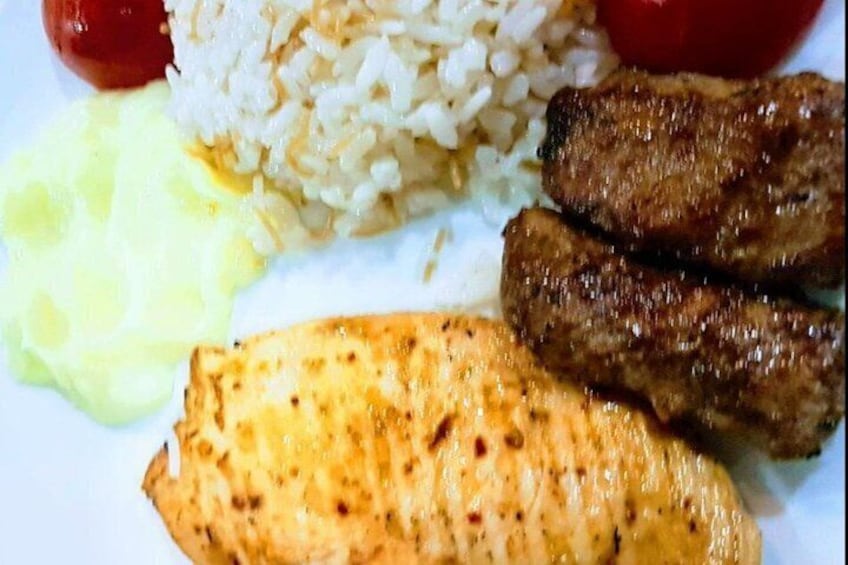 A plate with rice, grilled meat, a slice of fish, and a red tomato. 2