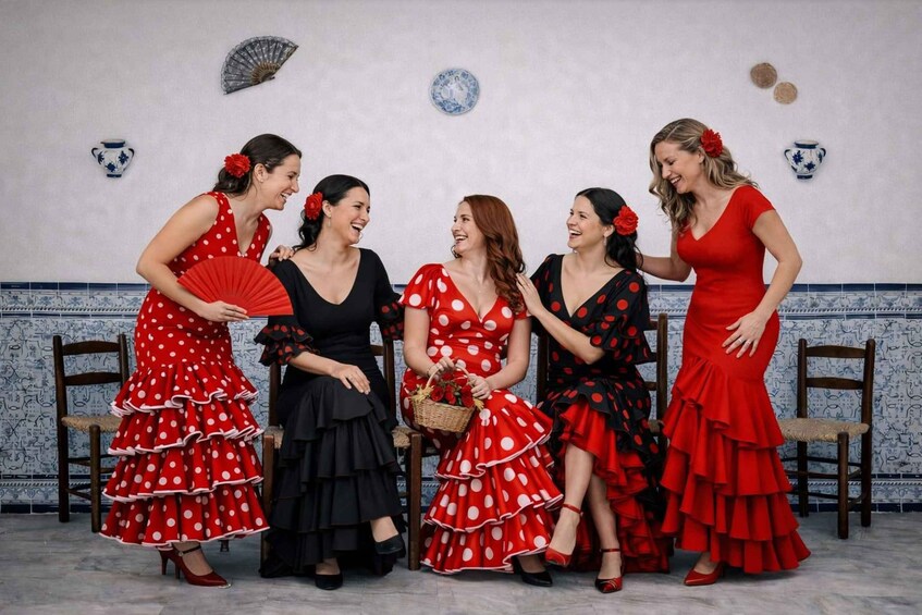 A group of women in polka dot dresses, some holding fans, in a room with tiled walls and decorative plates. 1