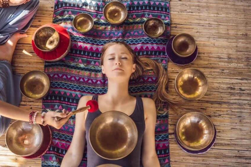 A person lying on a colorful mat surrounded by several large bowls. 2