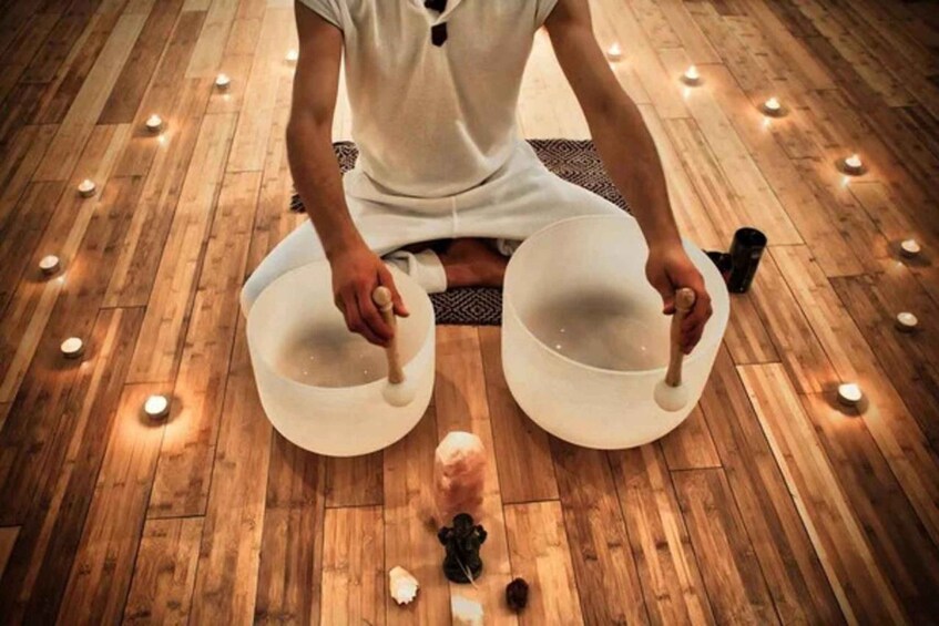 A person sitting on a mat, holding two bowls, with candles and scattered items on the floor. 3