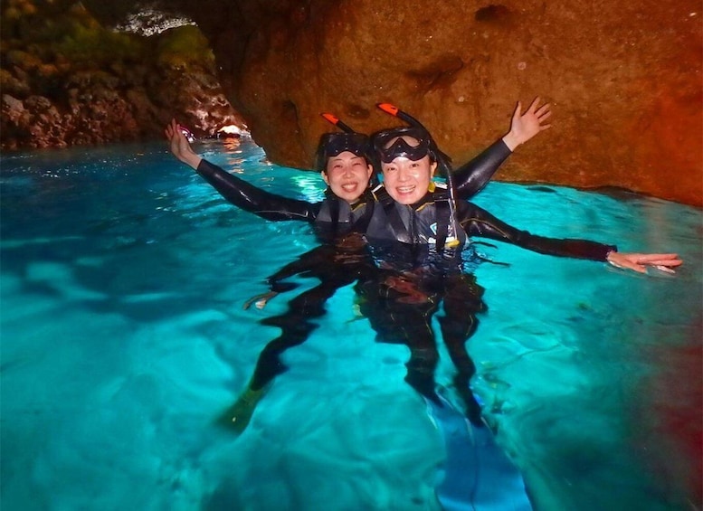 Two people scuba diving in a clear blue pool with rocky walls. 4