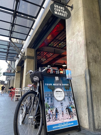 A bicycle parked in front of a building with a sign reading 'Grand Central Market' and a poster advertising bike tours. 5