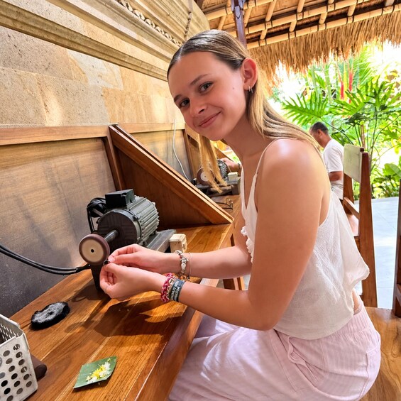 A person working at a wooden table with a motor and tools, in a setting with a thatched roof and greenery. 1
