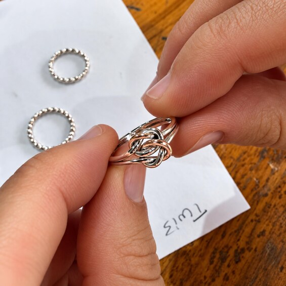 A person holding a silver ring with a complex design, with two other rings in the background. 4