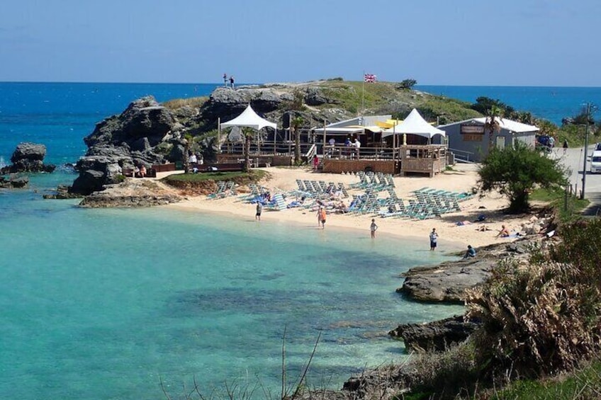A beach with clear turquoise water, a rocky outcrop, and a building with a white roof. 1