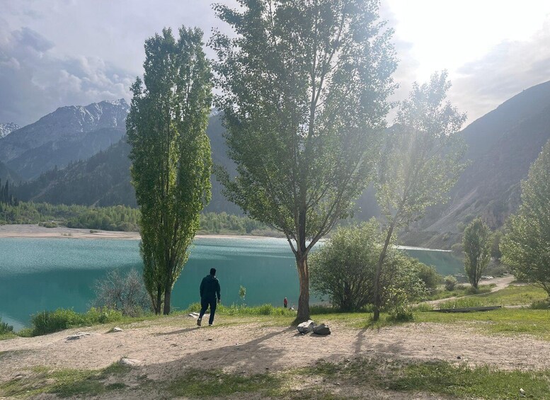 A person walking along a dirt path beside a lake with mountains in the background. 1