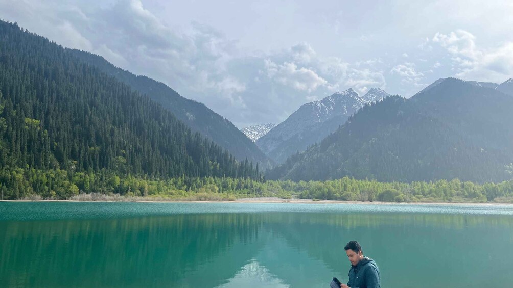 A person standing by a calm lake with mountains in the background. 4