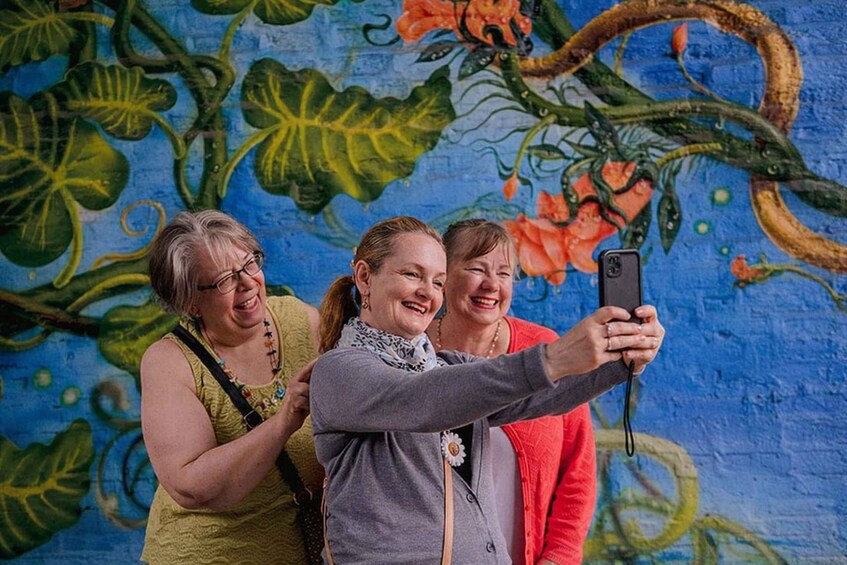 Three people taking a selfie in front of a colorful mural. 2