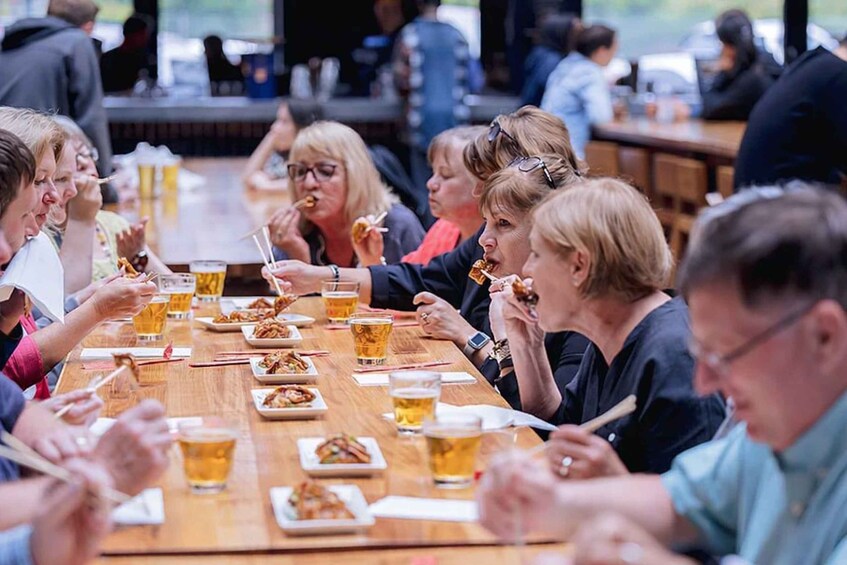 A group of people dining at a long wooden table with food and drinks. 4