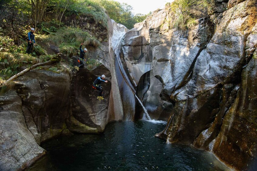 A group of people rappelling down a rocky cliff into a water-filled crevice. 4