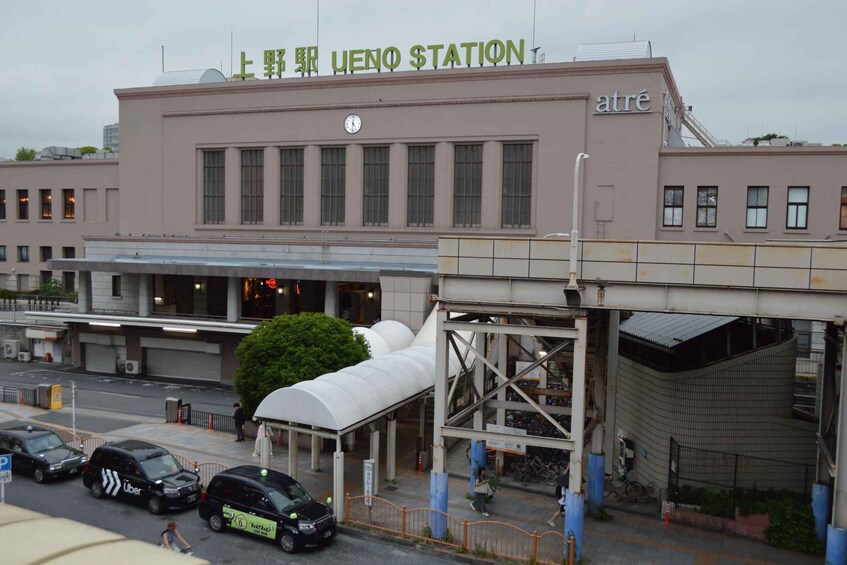 A train station with a sign reading 'UENO STATION' and a clock above the entrance. 2