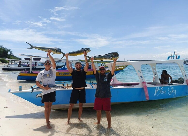 Three people holding fish on a beach with boats in the background. 1