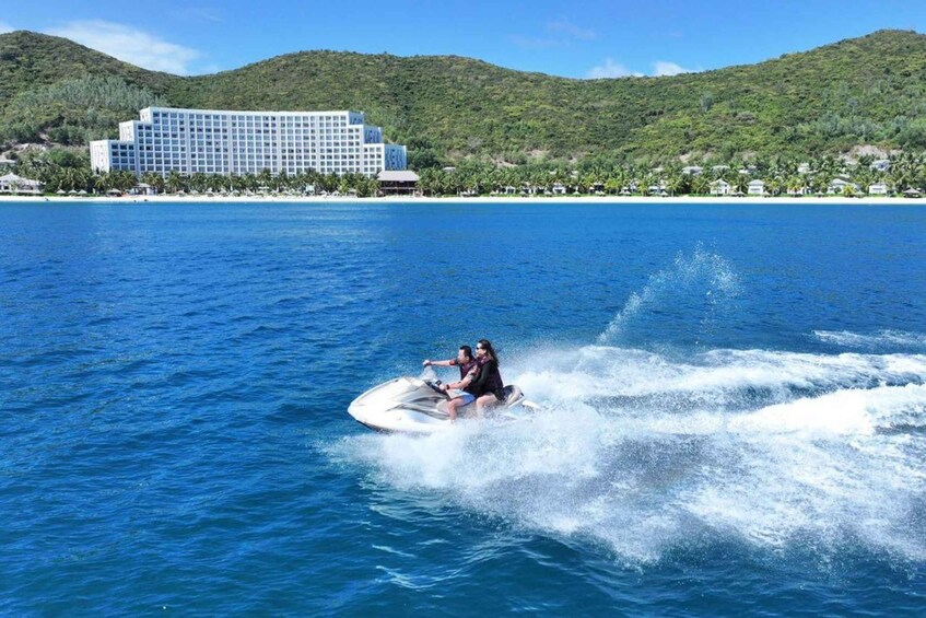 A person jet-skiing on a clear blue sea with a resort and hills in the background. 1
